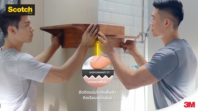 ผู้ชายกำลังติดตั้งชั้นวางของไม้บนผนังที่ทาสีและกรุด้วยกระเบื้อง
